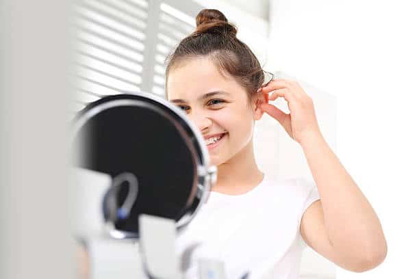 Cheerful girl assumes hearing aid viewing in the mirror