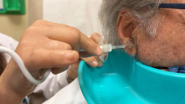 Senior caucasian man is at the doctor having wax removed from his ear.